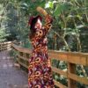 Mulher com vestido comprido e chapeu vermelho em zona arborizada numa ponte de madeira