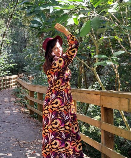 Mulher com vestido comprido e chapeu vermelho em zona arborizada numa ponte de madeira