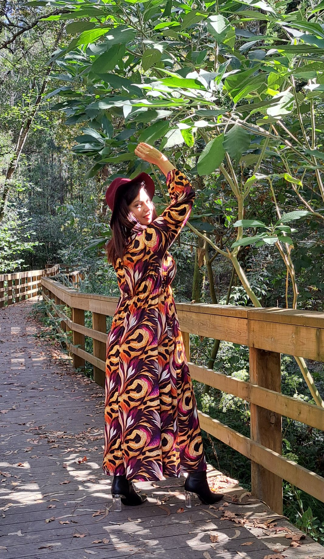 Mulher com vestido comprido e chapeu vermelho em zona arborizada numa ponte de madeira