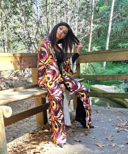 Mulher com roupa preta e um kimono colorido rodeada de árvores num banco de madeira