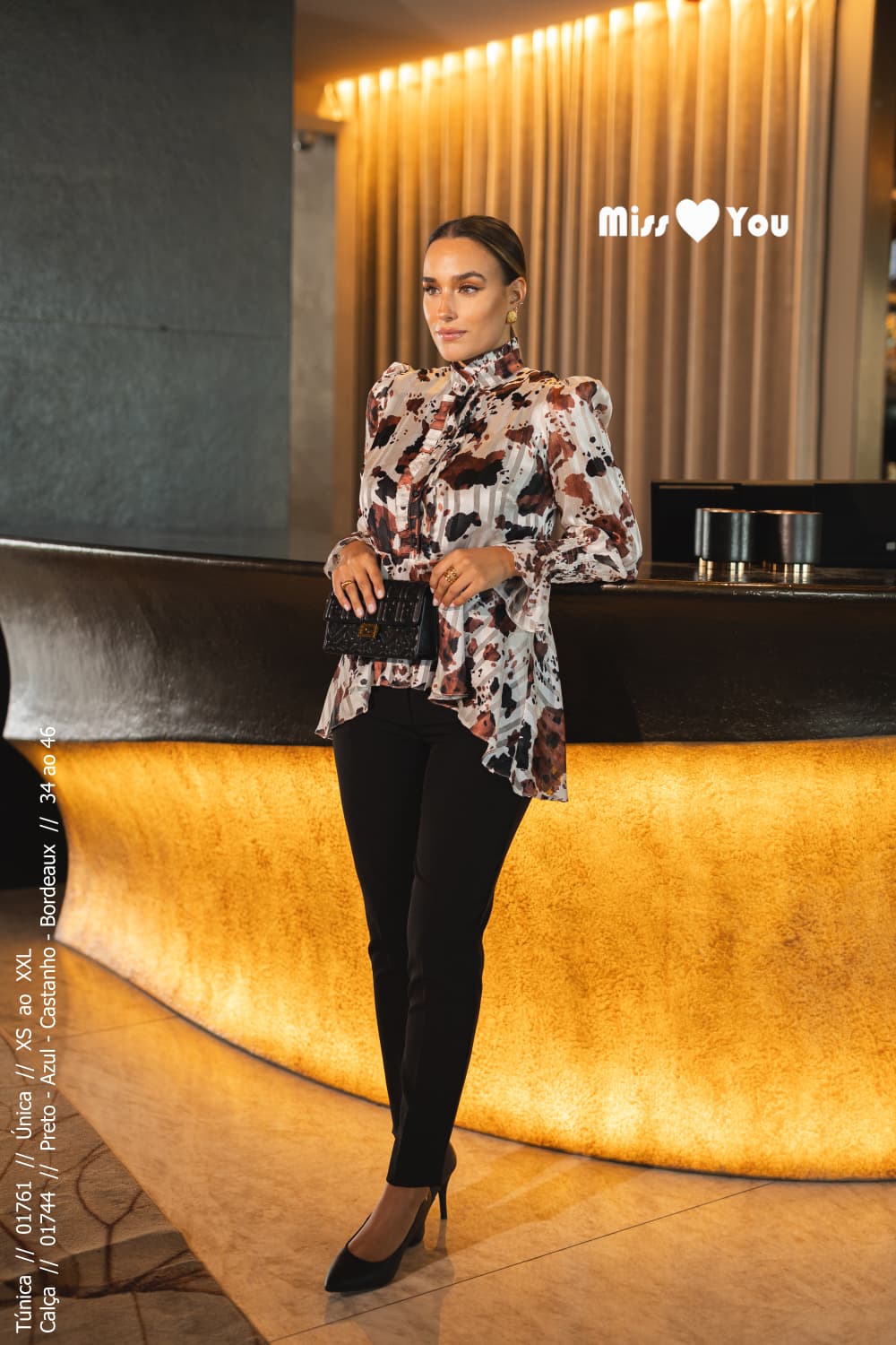 Mulher de cabelo apanhado perto de um balcão luxuoso com uma blusinha estampada da Miss You